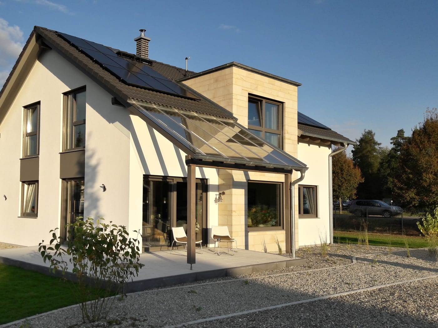Das Musterhaus Günzburg von der Terrassenseite im Abendlicht: Satteldach mit Photovoltaik, verglastes Vordach über der Terrasse und ein Vorbau mit Sandsteinfassade